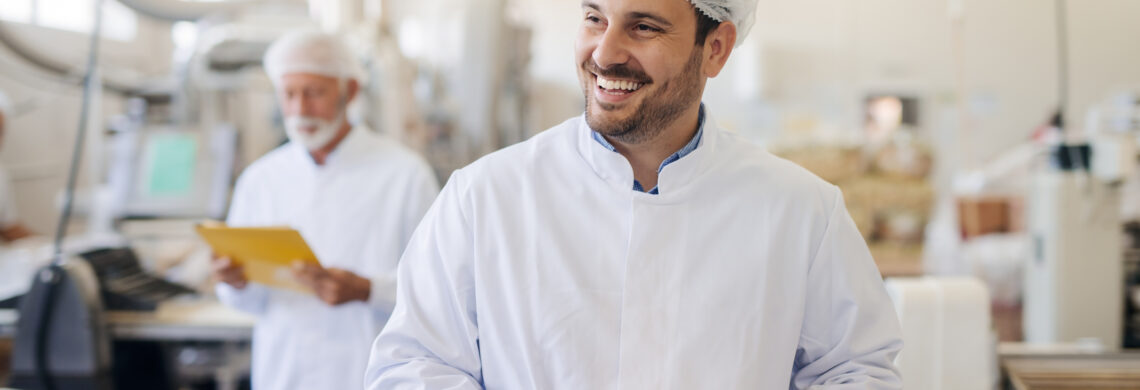 Smiling man using tablet while standing in food factory.